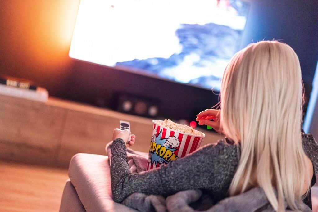A lady eating popcorn while watching tv